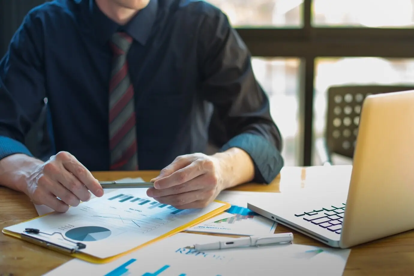 Business documents on an office table, with a business graph and social network diagram, while a man works in the background.